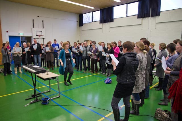 grote groep zingende docenten in een gymzaal, met Ellen Bakker als workshopleider